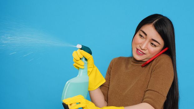 Asian housekeeper using duster and protective gloves to clean house