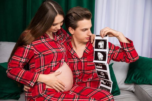 An expectant couple looks at and shows pictures of an ultrasound scan.