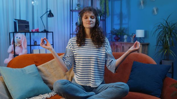 Young woman at home couch meditating with eyes closed with concentrated thoughts, listening music