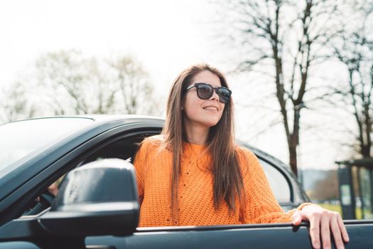 Caucasian young woman with long hair stepping out of her car on a sunny day