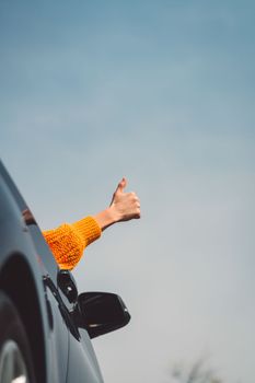 Vertical photo of persons hand sticking out the car window holding thumbs up