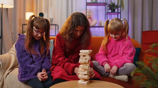 Three siblings children girls playing with blocks board game, build tower from wooden bricks at home