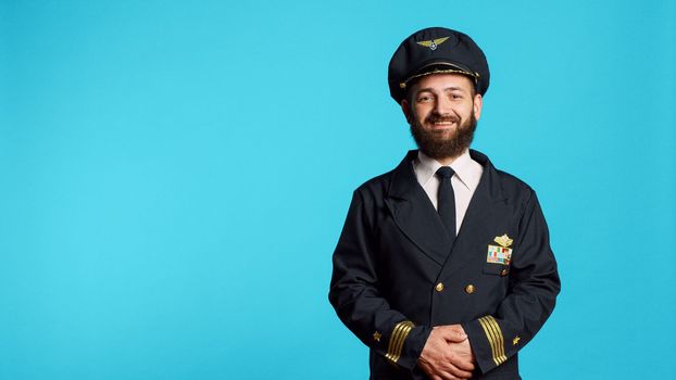 Male plane captain wearing airline uniform and posing in studio, having professional occupation. Young adult working as pilot to fly airplane, being cheerful and positive on camera.