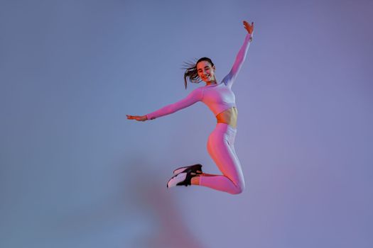 Smiling sporty woman in sportswear jumping on studio background. Sport and healthy lifestyle