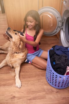 Chore day is childs play. a young girl doing laundry at home while her dog keeps her company.