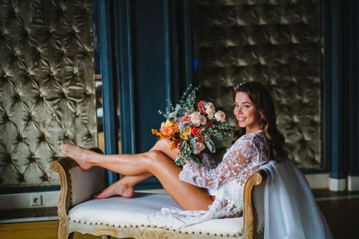 Seductive young bride posing with gorgeous bridal bouquet on a sofa