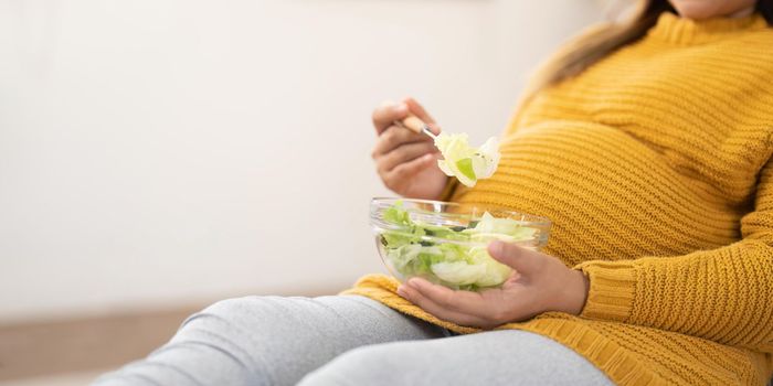 Happy pregnant young woman sitting and eating salad at home