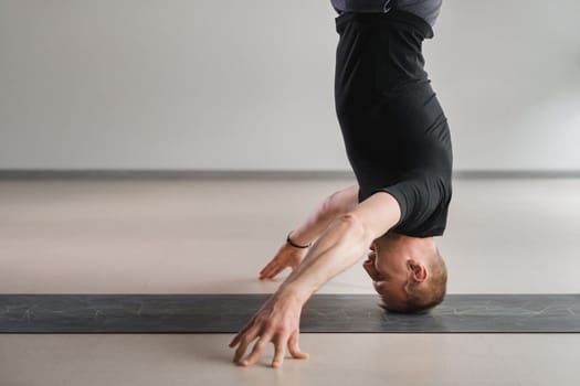 A man performs a yoga pose with support on his head in the gym. Yogi in a headstand
