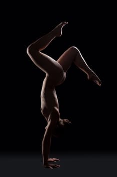 Nude gymnast posing in dark studio on hands