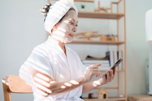 Portrait of elderly woman doing face spa treatment and using mobile phone.