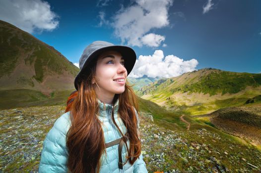 Portrait of a smiling woman resting during a mountain hike. A woman with a backpack enjoys the view while standing in the mountains. Happy tourist