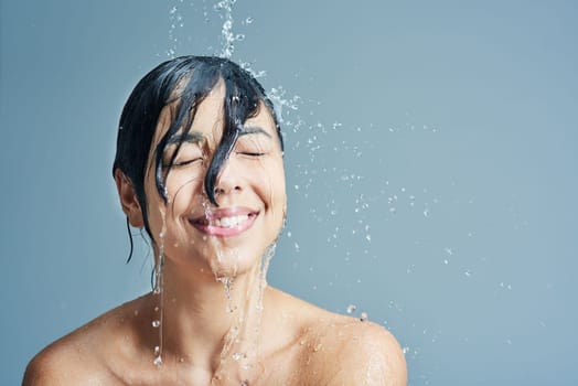 Awakening her senses with a refreshing shower. a young woman having a refreshing shower against a blue background.