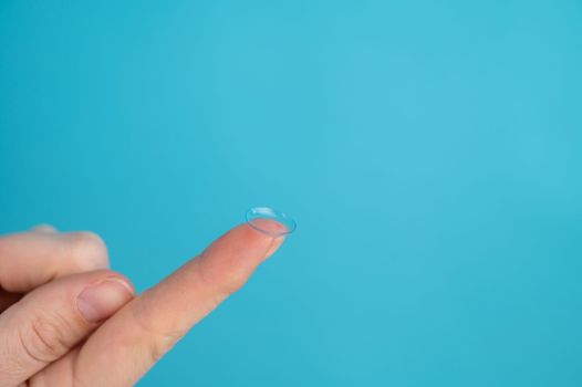 Woman holding contact lens on blue background.