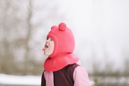 Funny little girl eating snow on winter day. Kids cold and flu concept. Tongue in snow.
