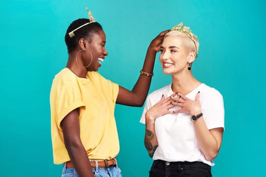 Everyones a winner when we empower each other. Studio shot of a young woman putting a crown on her friend against a turquoise background.