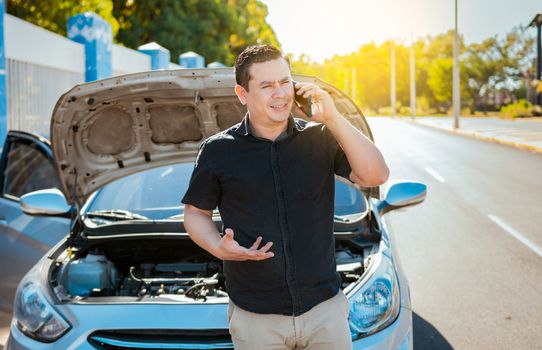 Young man with damaged car calling the mechanic, Frustrated man with damaged car calling technician on the road. Driver with the damaged car calling the mechanic