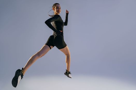 Smiling sporty woman running in Mid-Air exercising during cardio workout over studio background