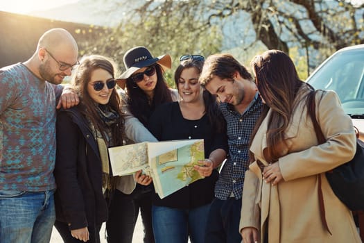 Friends are the best traveling buddies. a group of friends looking at a map while on a road trip