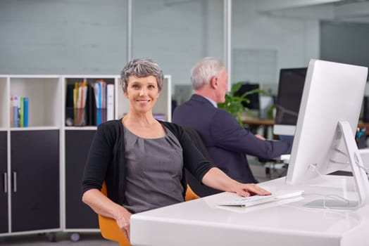 Shes confident in her position in this company. Portrait of a smiling mature businesswoman at her desk with a coworker in the background.