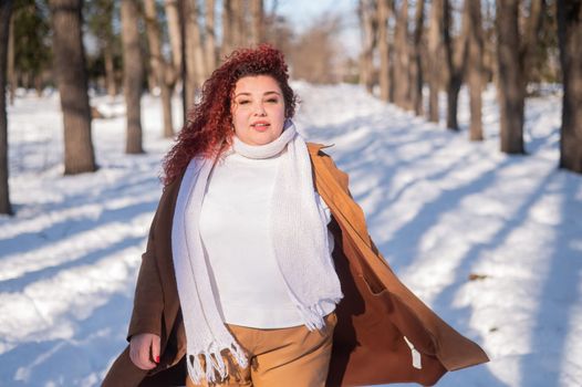Portrait of an excited red-haired curly fat woman in the park in winter.