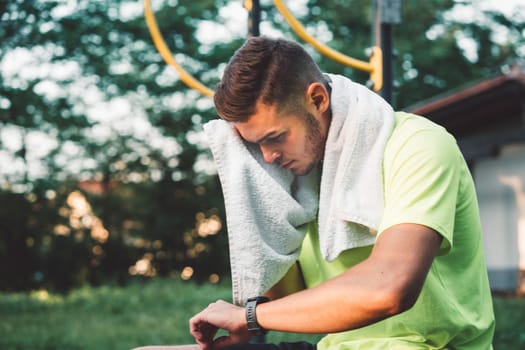 Young man looking down at his sports watch after his training, while wiping away the sweat