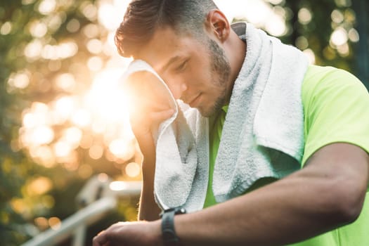 Sun flare across a young man wiping his sweat away while looking at his watch