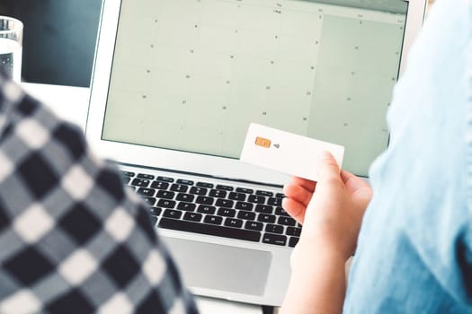 Over the shoulder view person holding a credit card open laptop screen with calendar in the background