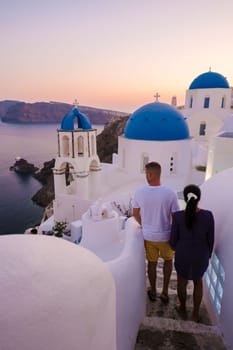 Men and women visit the whitewashed Greek village of Oia during vacation in Santorini with blue dome