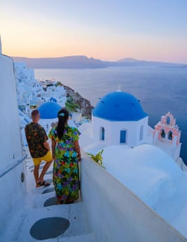 Men and women visit the whitewashed Greek village of Oia during vacation in Santorini with blue dome