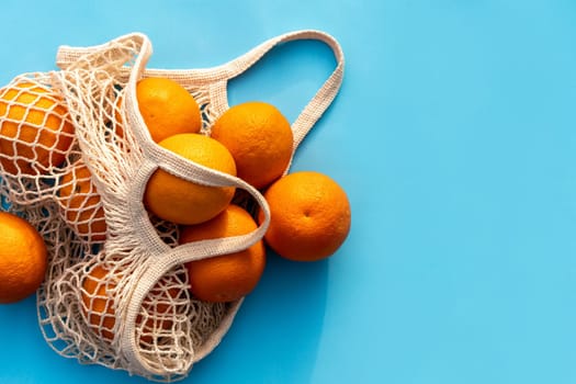 Mesh white cotton reusable bag with oranges on a blue background. Eco-friendly shopping. Space for text