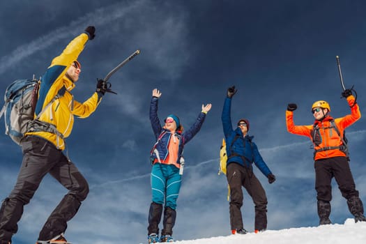 Low angle view, group of hikers jumping in the air when reaching the top of the snowy mountain