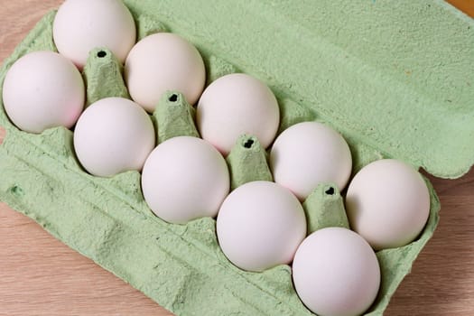 Fresh whole white eggs in green paper packaging on a wooden table