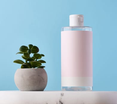 Blank bottle for cosmetics with pink paper label on a blue background. Bottle for tonic, gel