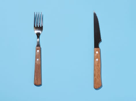 Fork and knife with wooden handle on blue background, top view