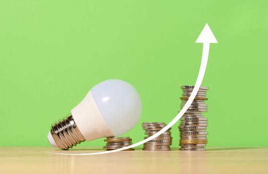 A stack of coins and a glass lamp on a green background, up arrow. The concept of the growth of new ideas in business, high income. Rising electricity prices