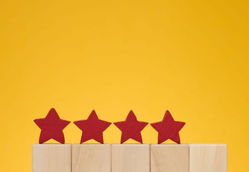 Four stars on wooden cubes, yellow background. Service evaluation concept, high rating