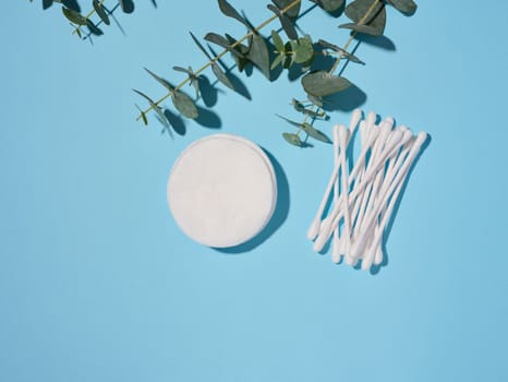 Round cotton cosmetic pads and cotton buds on a blue background, top view