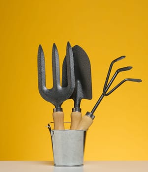 Miniature garden tools in a metal bucket on a yellow background