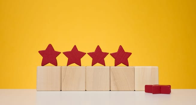 Four stars on wooden cubes, yellow background. Service evaluation concept, high rating