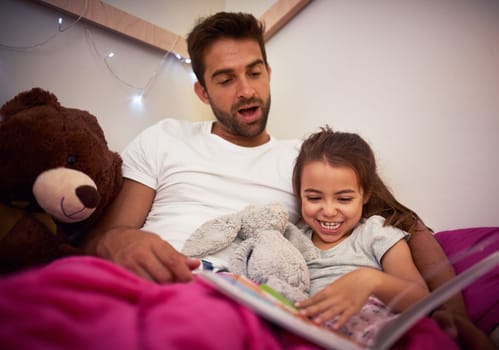 Theyre always having fun, right up to bedtime even. a father reading a book with his little daughter in bed at home