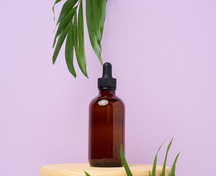 A brown glass bottle with a pipette on purple background. Containers for cosmetics