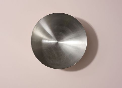 Empty round metal bowl on beige background, top view