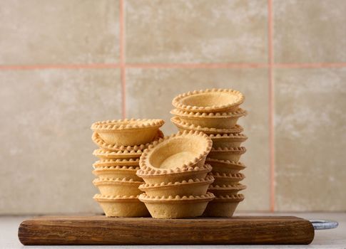 Stack of empty baked round canape baskets on a wooden board, round empty tartlets