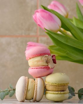 Baked macarons with different flavors on the table, behind a bouquet of tulips