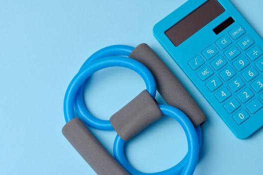 Rubber sports simulator expander and a calculator on a blue background, top view, calorie counting