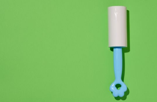 Roller with sticky tape for cleaning clothes on a green background, top view