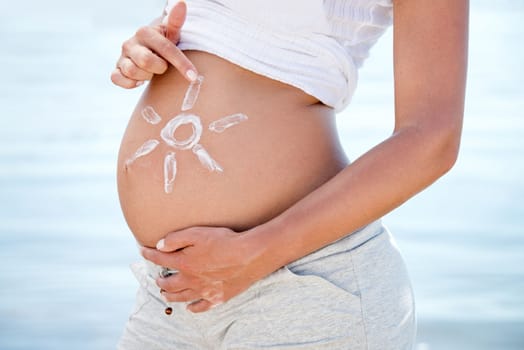 Belly bonding. a pregnant woman with the sun drawn onto her belly against the background of the ocean.