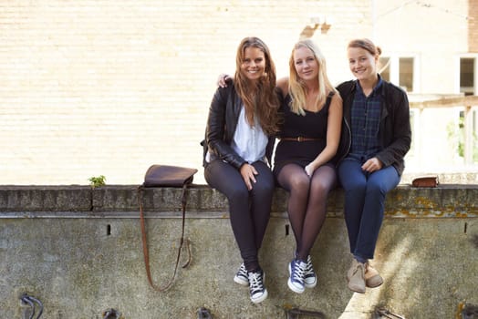 Surviving the teenage years together. Three teenage girls sitting on a wall smiling at the camera.