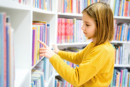 Schoolgirl choosing book in school library.