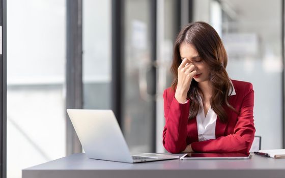 business woman stressed ,suffering headache or migraine with laptop computer and papers working